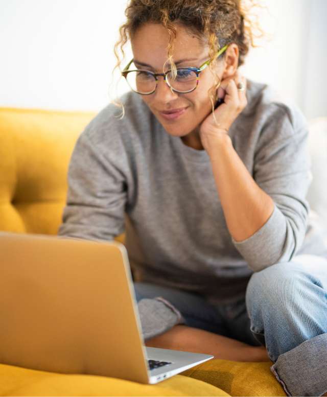 Woman sitting on a yellow sofa using a laptop