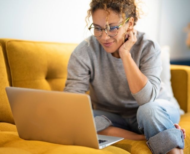 Female sitting on a yellow sofa using a laptop